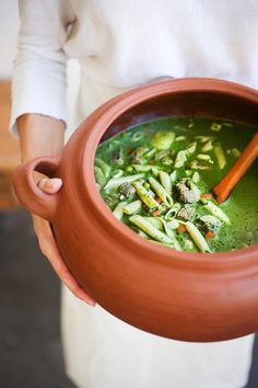 a person holding a pot filled with green soup and vegetables in it's hands