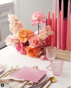 the table is set with pink and orange flowers, candles, and napkins on it