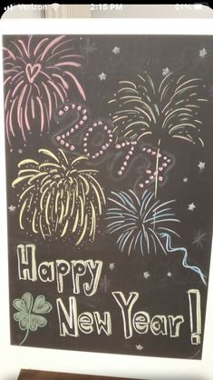 a chalkboard sign with fireworks and stars on it that says happy new year in front of a wooden floor