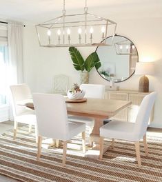 a dining room table with white chairs and a round mirror above it on the wall