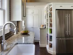 a stainless steel refrigerator and sink in a kitchen with marble counter tops, white cabinets and wooden flooring