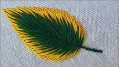 a green and yellow leaf is sitting on a piece of fabric, with some thread attached to it