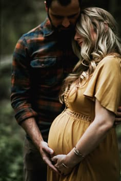 a pregnant couple cuddles in the woods while holding each other's belly