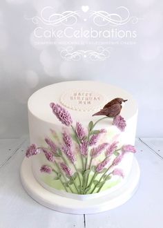 a birthday cake decorated with lavender flowers and a bird on top is shown in front of a white background