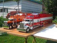 three toy trucks are sitting on a table in front of a house and fenced yard