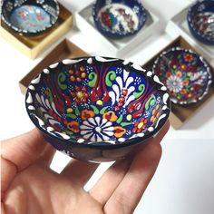 a hand is holding a colorful bowl in front of several other bowls with designs on them