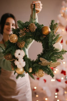 a woman holding up a christmas wreath with ornaments on it