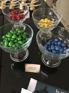 three glass bowls filled with candy on top of a black counter next to a sign