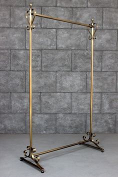 a gold metal frame with two legs and an iron bar on the bottom, against a gray brick wall