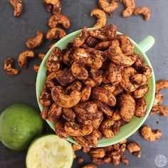 a green bowl filled with cashews next to a lime