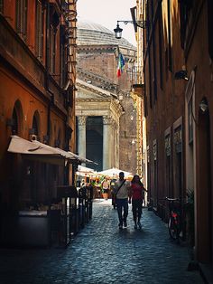 two people walking down an alley way between buildings