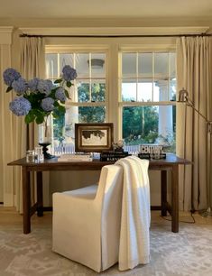 a white chair sitting in front of a window next to a table with flowers on it