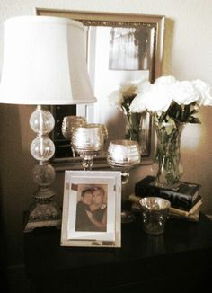 a table with a lamp, vases and pictures on it in front of a mirror