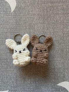 two crocheted bunny keychains sitting next to each other on a gray surface