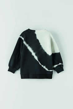 a black and white tie dye sweatshirt with long sleeves, on a hanger against a wall