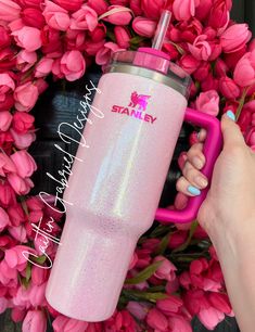 a person holding a pink tumbler in front of some tulips with the name stanley on it