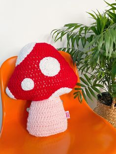 a crocheted mushroom hat sitting on an orange chair next to a potted plant