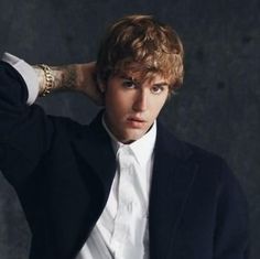 a young man in a black suit and white shirt is posing with his hands on his head