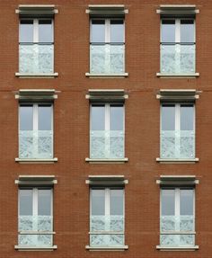 an orange brick building with many windows on each side and white balconies above the windows