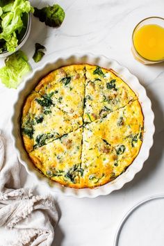 a quiche with cheese and spinach on a white table next to some salad