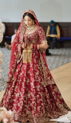 a woman in a red and gold bridal gown is walking down the aisle with her hand on her hip