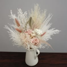 a white vase filled with flowers and feathers on top of a wooden table next to a gray wall