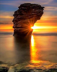 the sun is setting behind a rock formation in the ocean with water reflecting off it's surface