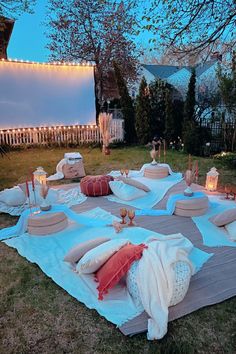 an outdoor movie set up with pillows, blankets and candles on the grass in front of a house