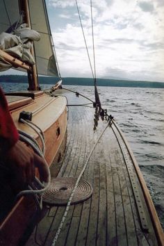 the front end of a sailboat with ropes on it's deck and water in the background