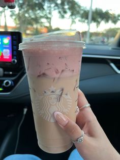 a woman holding up a cup of coffee in her hand while sitting in the driver's seat of a car