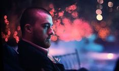 a man sitting on a bench in front of a city street at night with colorful lights