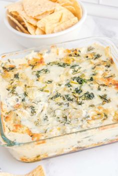 a casserole dish with spinach, cheese and tortilla chips on the side