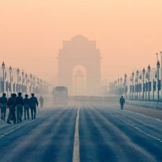 people are walking down the street in front of an arch on a foggy day