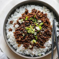 a bowl filled with rice, meat and vegetables next to chopsticks on a table