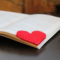 an open book with a red felt heart on the pages, sitting on a table