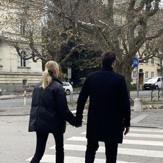 a man and woman walking across a street holding hands