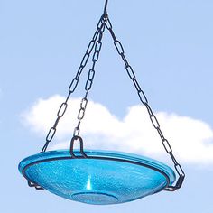 a blue glass bowl hanging from a chain with clouds in the sky behind it on a sunny day