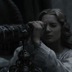 a woman looking through a telescope at something in the distance with her hand on it