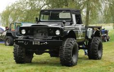 a large black truck parked on top of a lush green field next to a tent