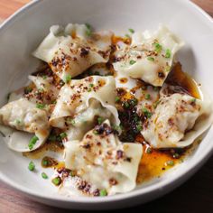 a white bowl filled with dumplings covered in sauce and topped with scallions