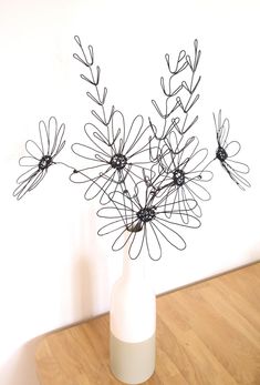 a white vase filled with black wire flowers on top of a wooden table next to a wall