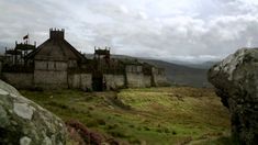 an old stone building sitting on top of a lush green hillside next to large rocks