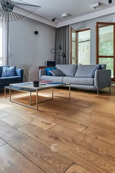 a modern living room with wood floors and blue couches in the corner, along with a chandelier hanging from the ceiling