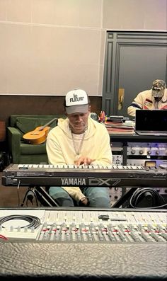 a man sitting in front of an electronic mixing console with two other people behind him