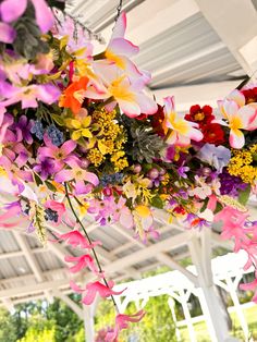 colorful flowers hanging from the ceiling in a white tented area with tables and chairs