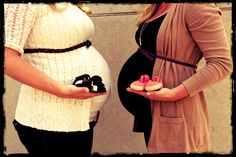 two pregnant women are holding small baby shoes