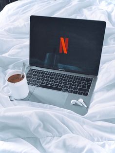 an open laptop computer sitting on top of a bed next to a cup of coffee