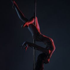 a woman in red is standing on a pole with her legs bent over the pole