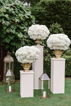 three vases filled with white flowers sitting on top of pedestals in the grass