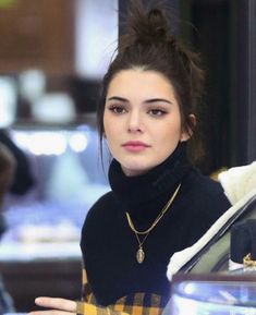 a young woman wearing a black turtle neck sweater and gold necklace is looking at the camera